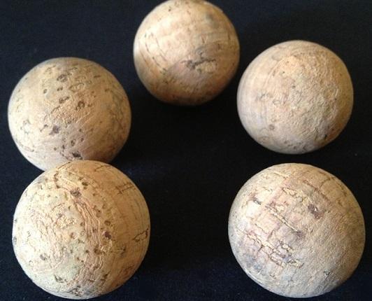 Five large natural cork balls with hole on a black background.