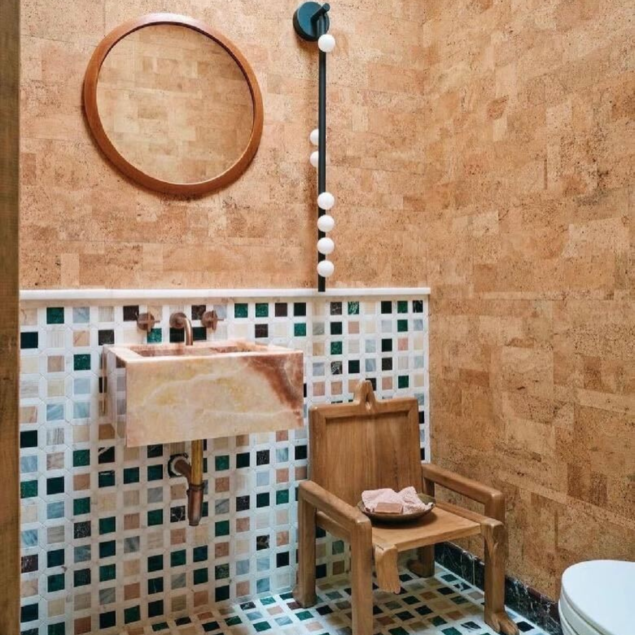 A half bath with teal tan and blue tile floor and part of the wall with the rest of the wall being covered in a natural colored cork tile. 