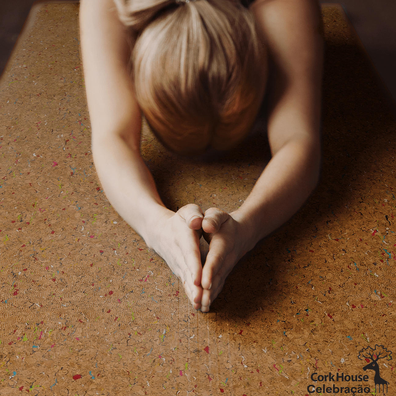 A blonde woman in childs pose on a cork yoga mat with a brigt confetti pattern on the top of the mat. 