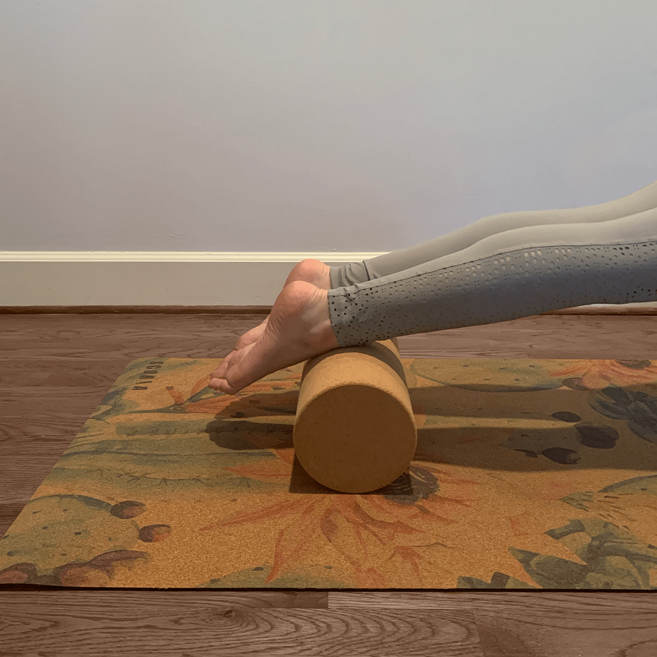 A woman balancing her ankles on a cork yoga cylinder to roll out muscles. 