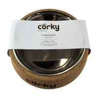 A stainless steel dog bowl in a natural cork holder with "corky" written in black on the front of the cork. The bowl is in a paper sleeve which says "corky by pelcor cork and stainless steel feeder"