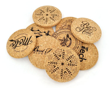 A pile of natural cork coasters with assorted printing. Patterns include, a snowflake, "bless your heart", a wineries logo and other business logos